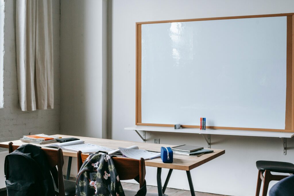 An empty classroom with wooden desks, chairs, and a large whiteboard for teaching.